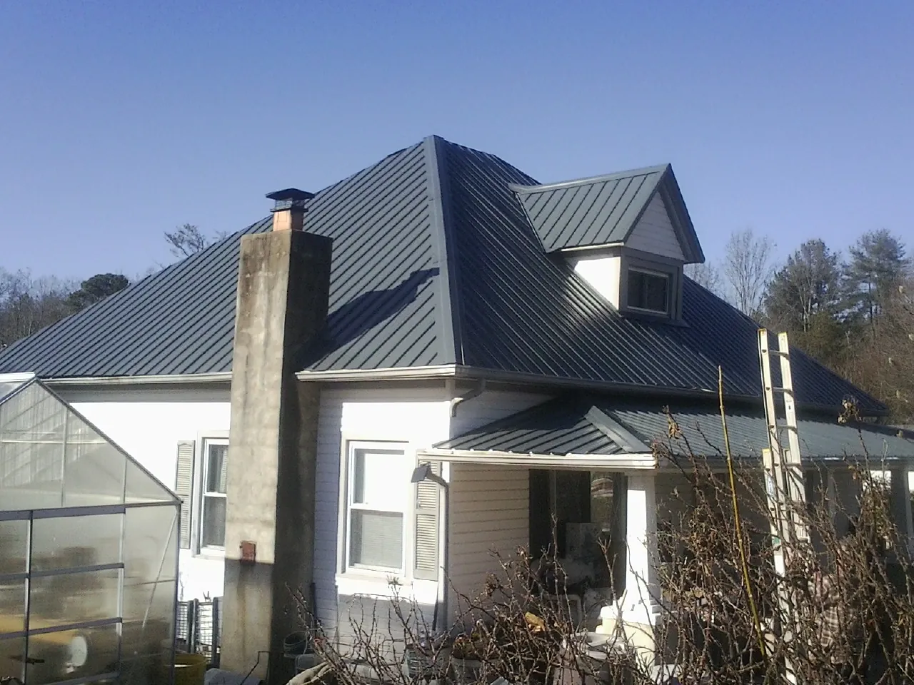 Dark blue standing seam metal roof on a white farmhouse with dormer — Slate & Tile Roof Repair by Roofing Brothers in Franklin Park
