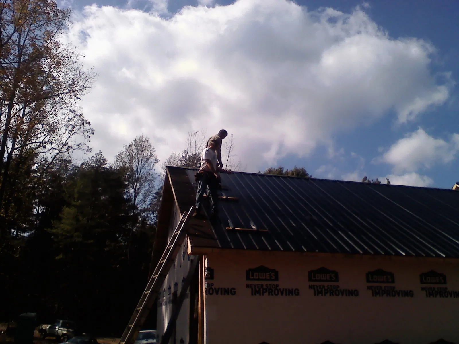 Roofer fastening dark metal panels high against a cloudy sky, from a Roof Inspection job in Franklin Park
