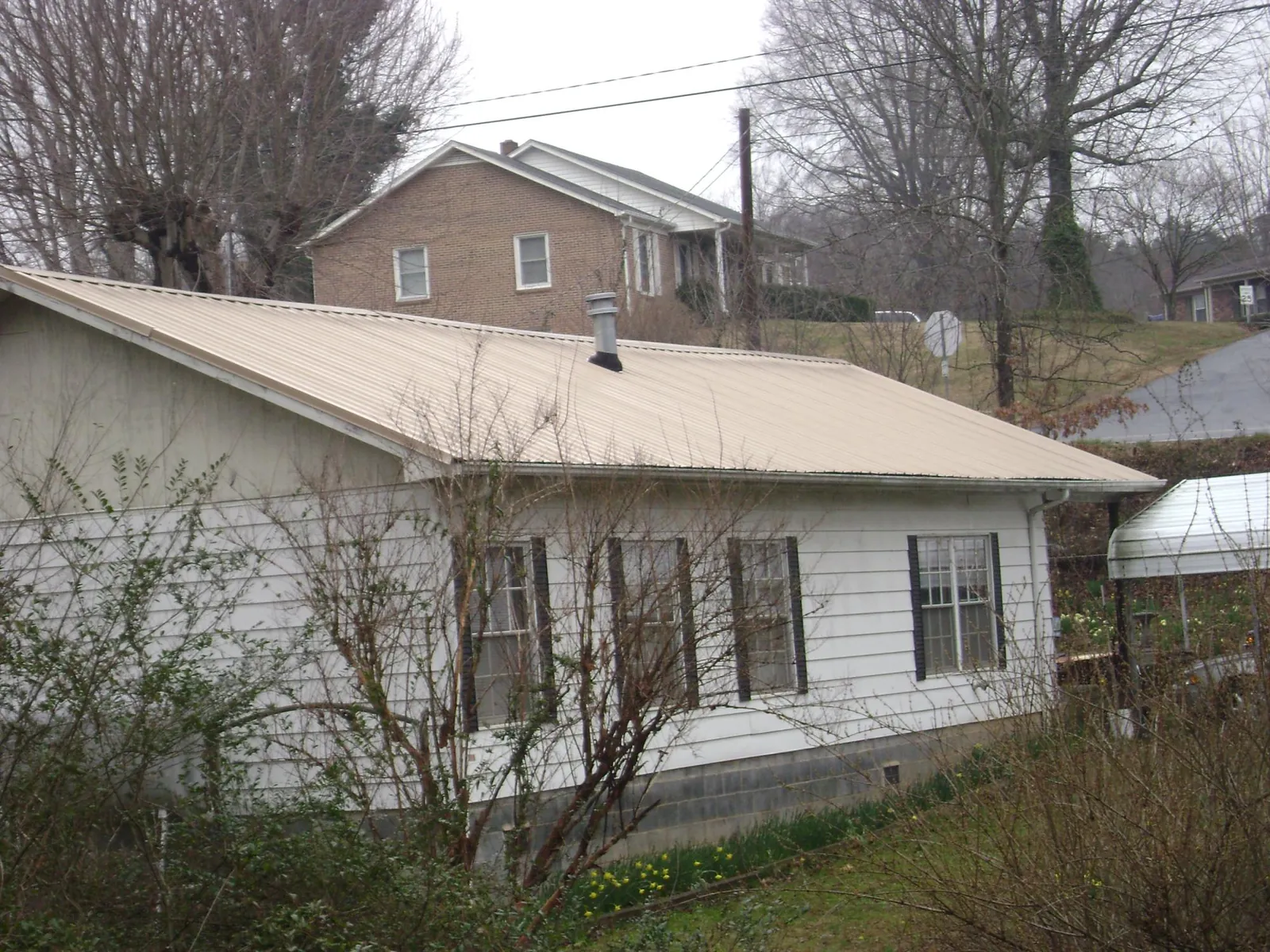 Tan metal roof on a white sided house set into a hillside — Commercial Roofing by Roofing Brothers in Franklin Park